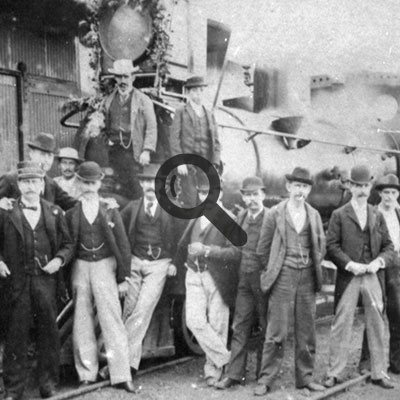 Foto antigua de 1894 de varios hombres con traje formal frente a una locomotora