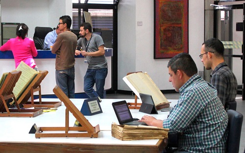 Foto de varias personas en la Sala de Consulta, 2 sentados revisando documentos, 3 en el mostrador