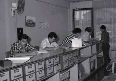 Foto antigua del archivo notarial: personas revisando documentos en el mostrador