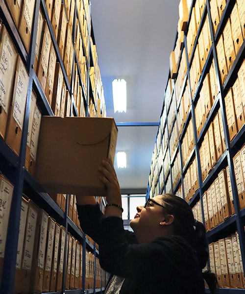 Foto de mujer acomodando caja de archivo en estantería metálica